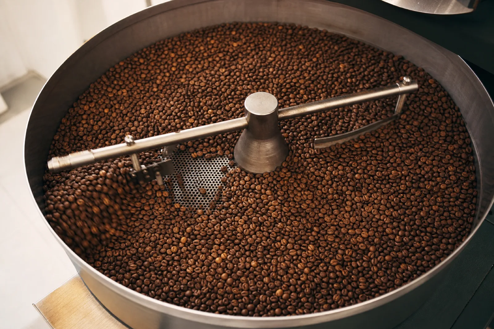 เมล็ดกาแฟที่เพิ่งคั่วเสร็จกระจายอยู่ในถาดพักที่มีแขนกวน