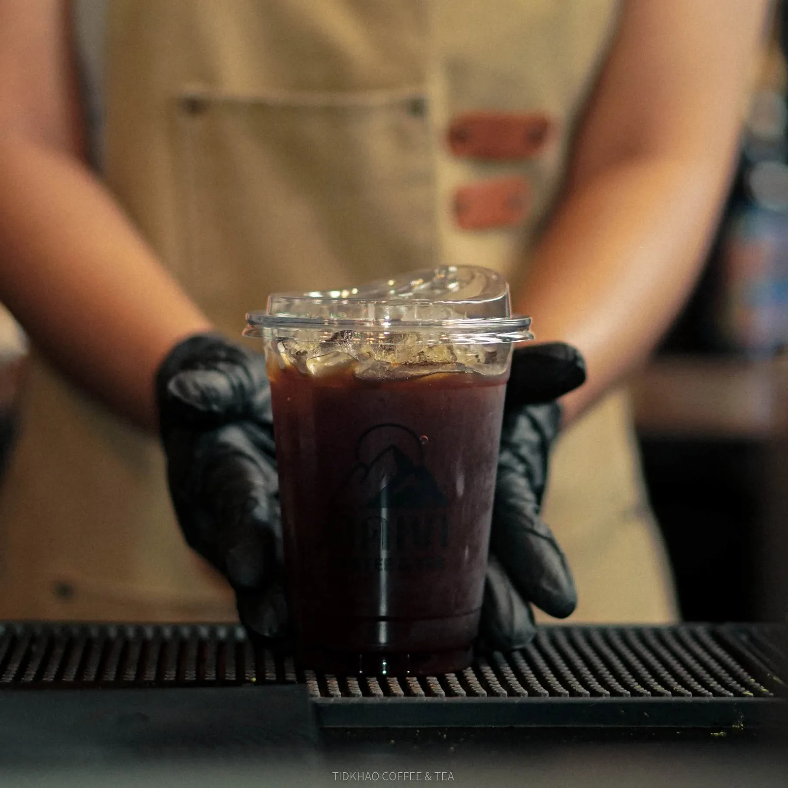แก้วกาแฟดำเย็นของร้าน ถือด้วยมือสวมถุงมือ